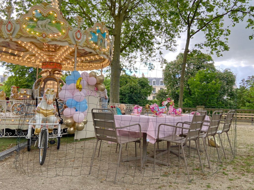 Birthday party table in front of a merry-go-round at Jardin Darcy in Dijon, France. 