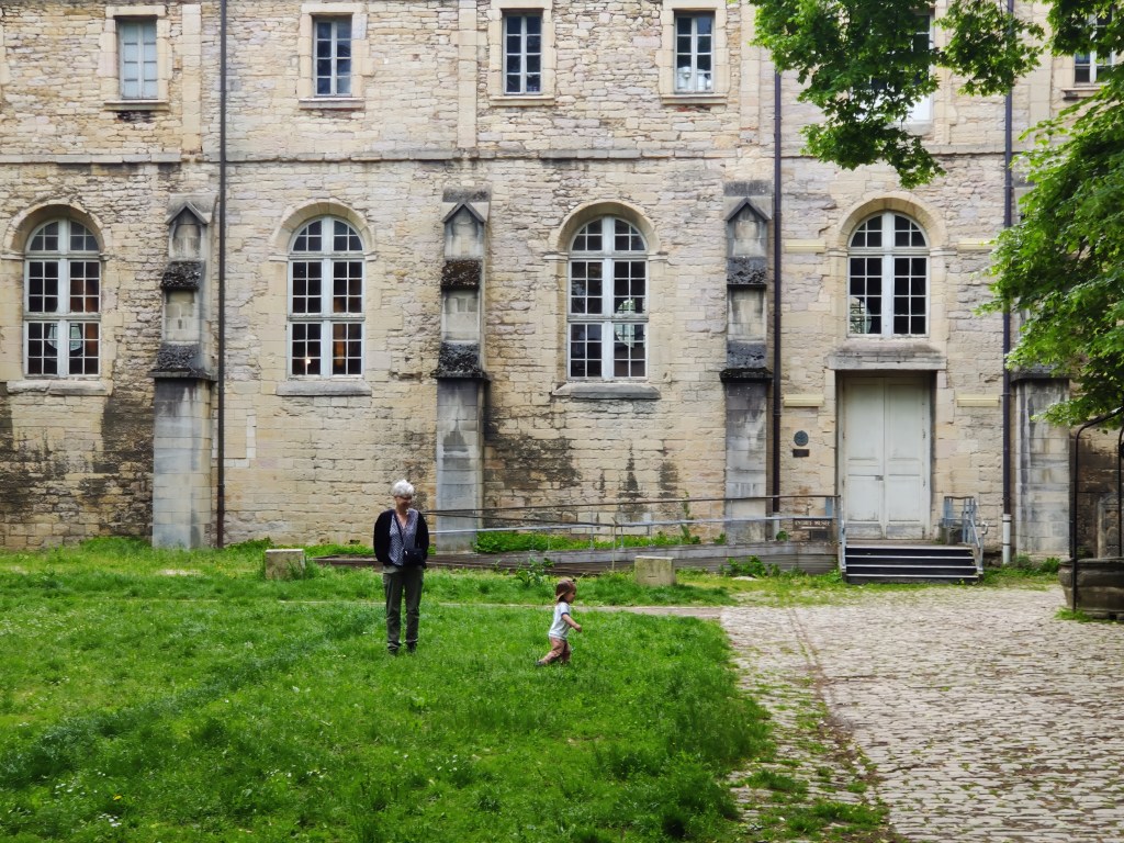 Toddler running in the grass in front of an old stone building in Dijon, France
