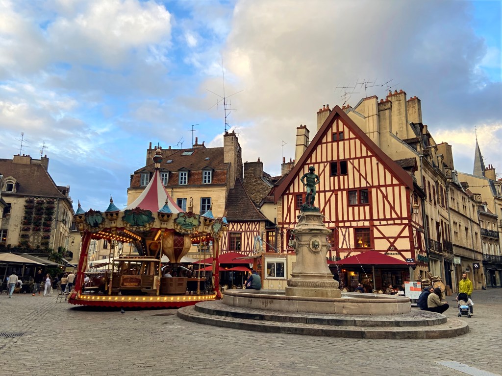 Old town Square in Dijon, France at dusk, showing the merry-go-round, fountain, and half timbered building. 